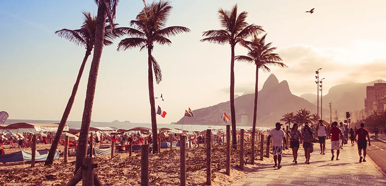 Pessoas caminhando em um final de tarde no calçadão de Copacabana, no Rio de Janeiro.